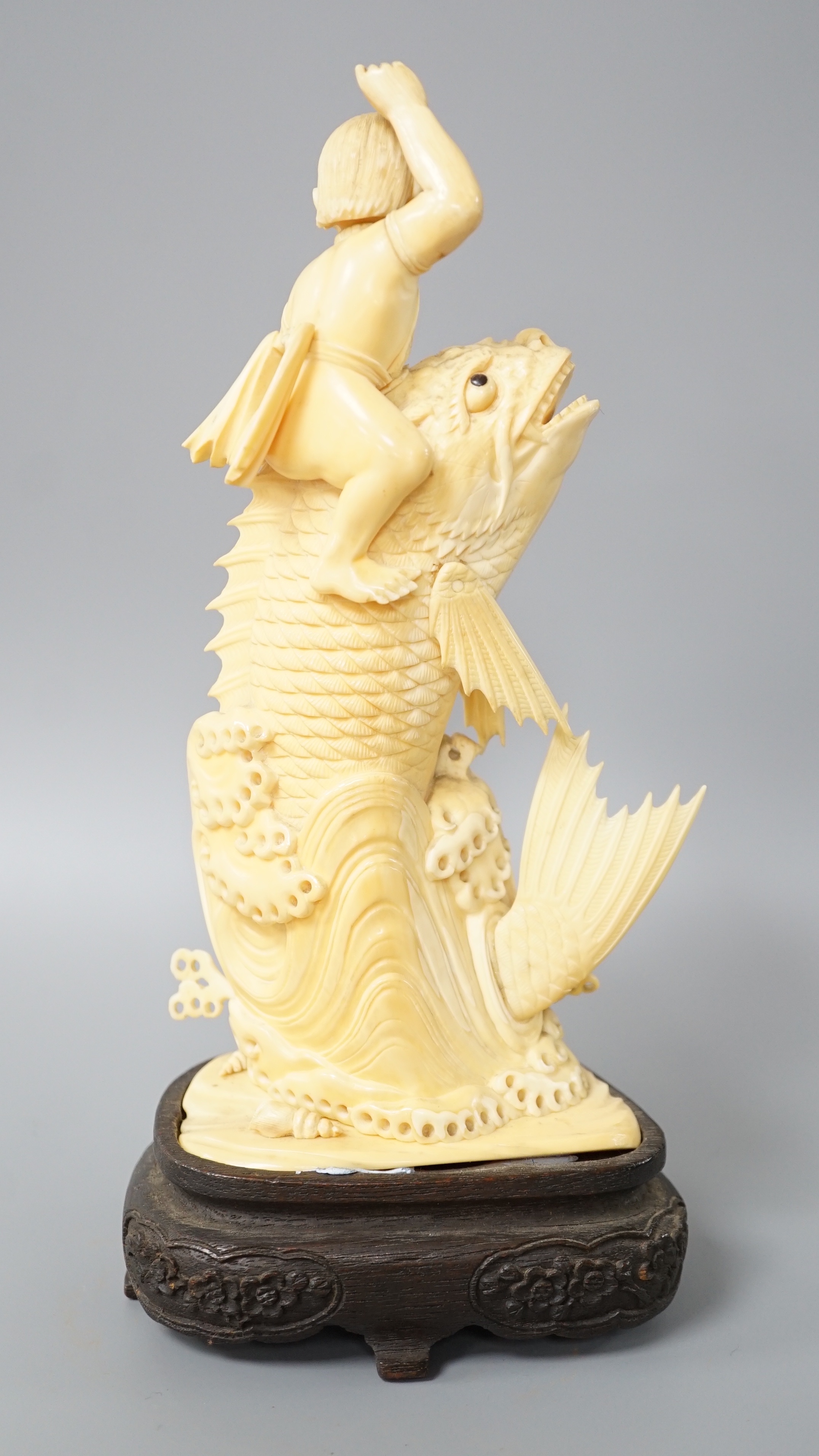 A Japanese sectional ivory okimono of a boy riding a leaping carp, early 20th century, wood stand, 25cm